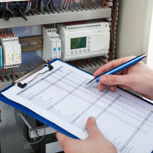 Electrician Holding Clipboard While Examining Fusebox