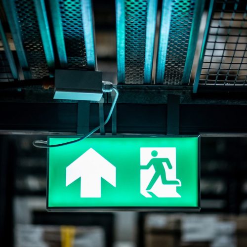 Green Emergency Exit Sign Or Fire Exit Sign Showing The Way To Escape With Arrow Symbol.