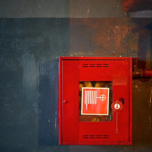 Fire Hose In Red Box. Pipe Roll For Fire Emergency In Red Metal Cabinet On Grey Oil Paint Concrete Wall With Multicolor
