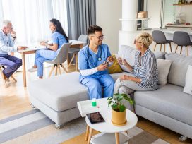 Male Nurse Talking To Seniors Patients While Being In A Home Visit.