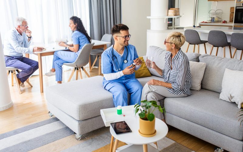 Male Nurse Talking To Seniors Patients While Being In A Home Visit.